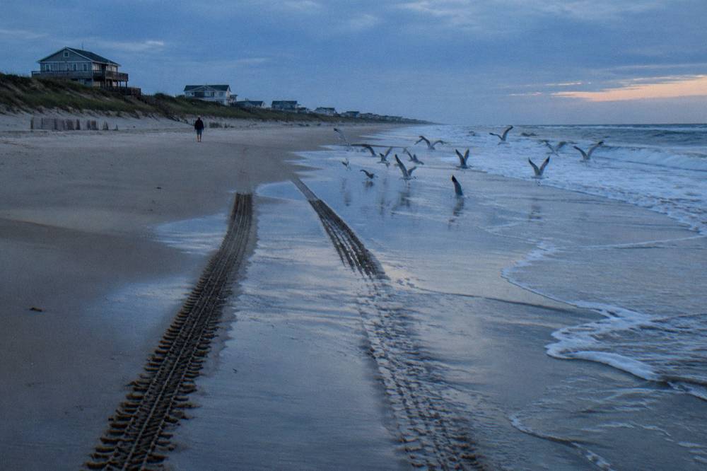 Tire tracks in wet sand at the base of a wide open beach