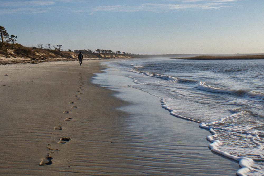 Long stretch of empty wet sand at the waterline curving north toward distant dunes
