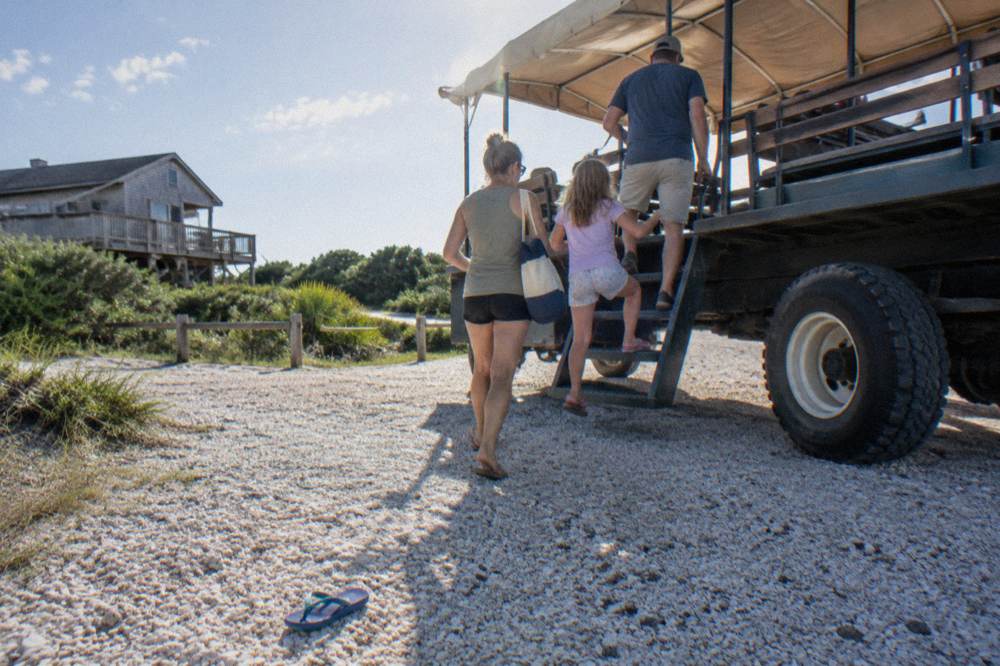Family boarding an open-air beach tour truck on a sunny afternoon in Corolla