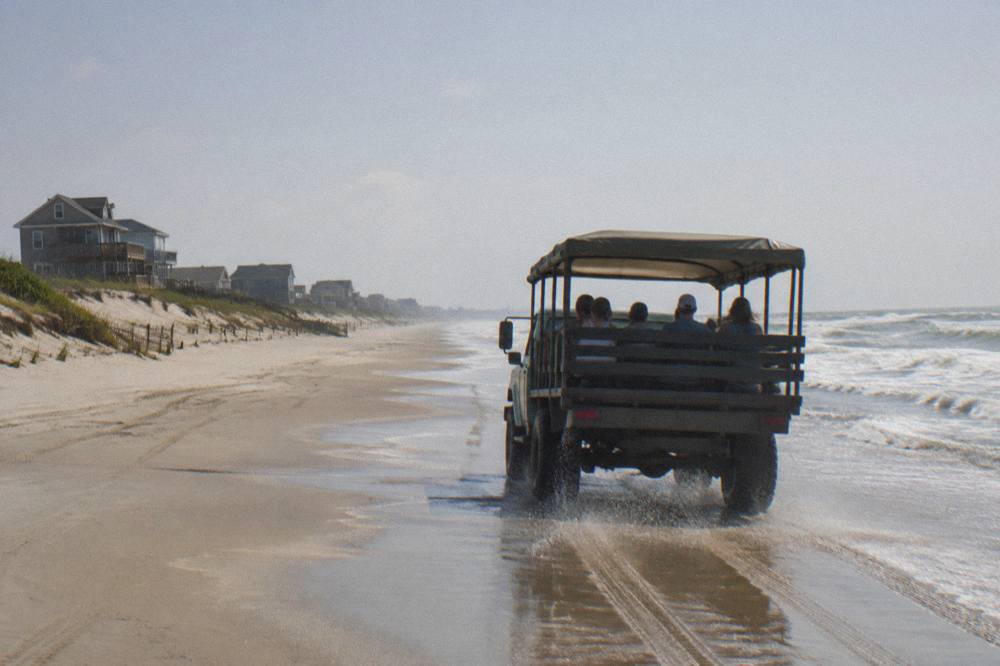 Open-air 4WD tour truck driving along the wet sand of the Corolla beach with the ocean on one side