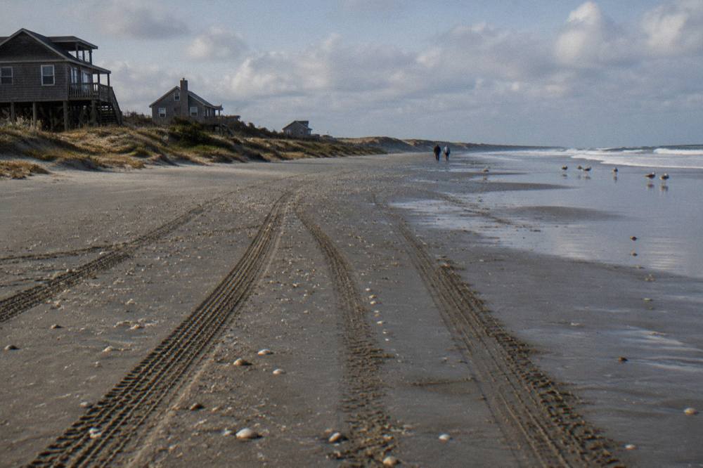 Wind-swept off-road beach with tire tracks in wet sand and distant dunes