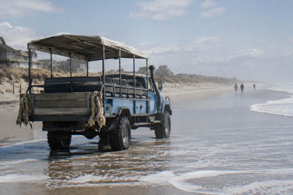 Open four-wheel-drive tour truck parked on wet sand at the water line