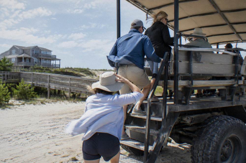 Small group of travelers seated in the open back of a four wheel drive tour truck on the beach