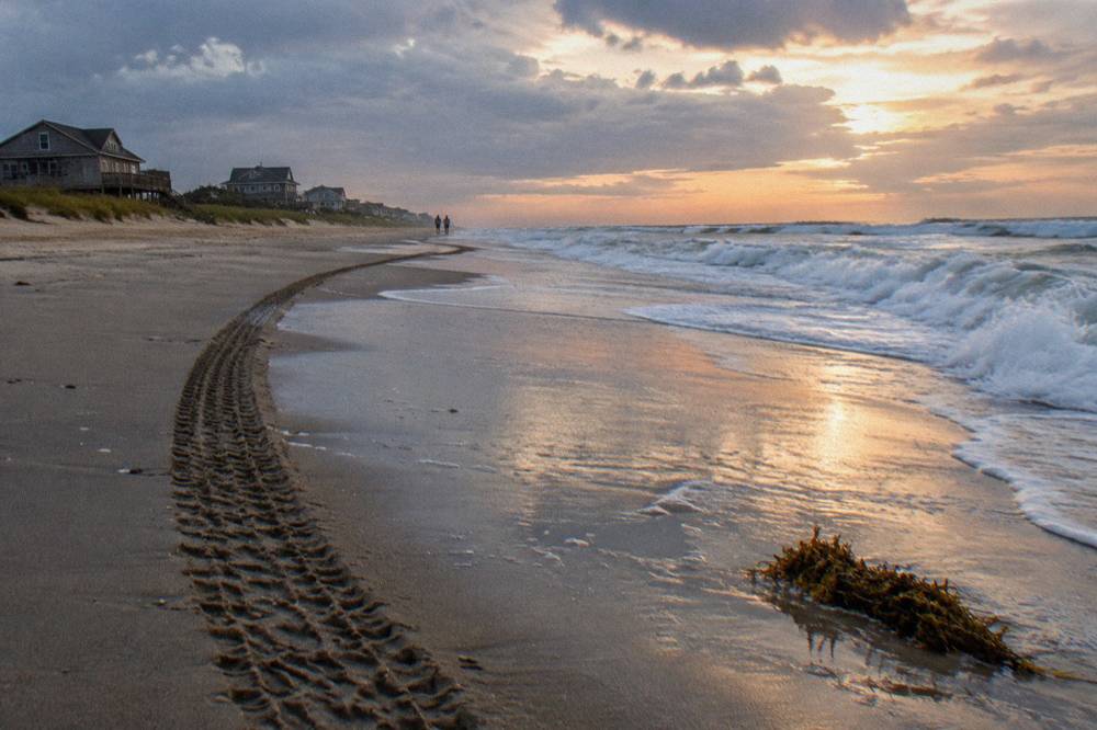 A wide truck tire track running along wet sand beside breaking waves on the Corolla beach
