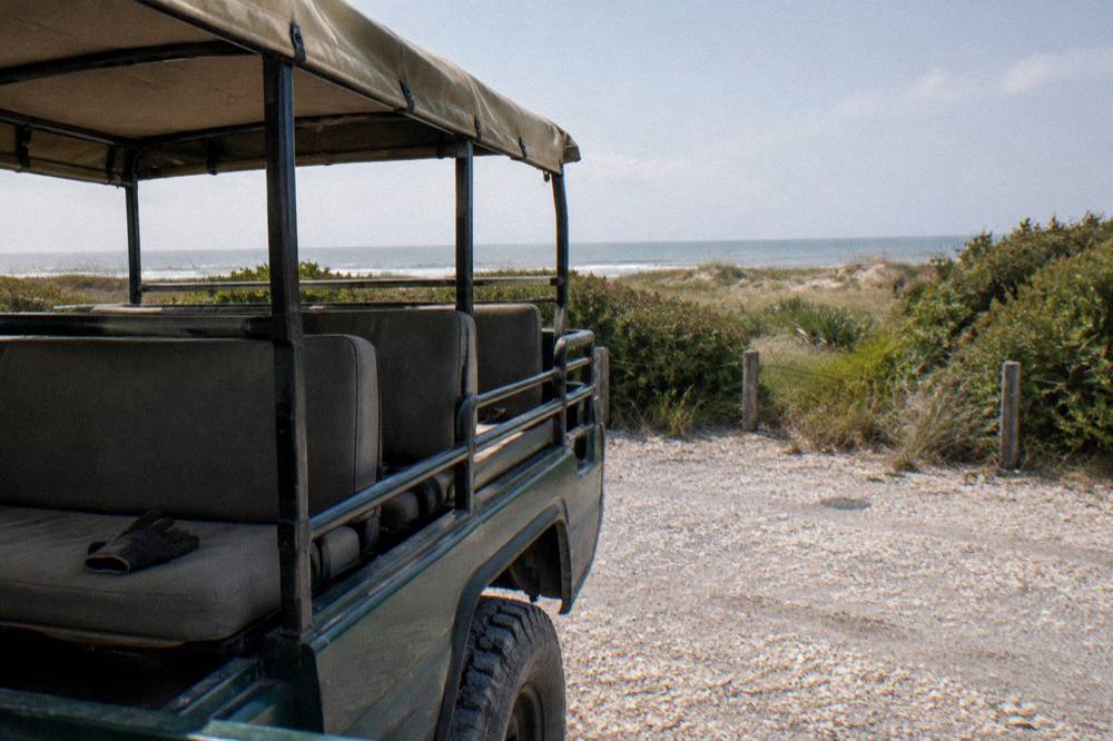 A guided open-air four wheel drive truck parked on the beach with dunes behind it