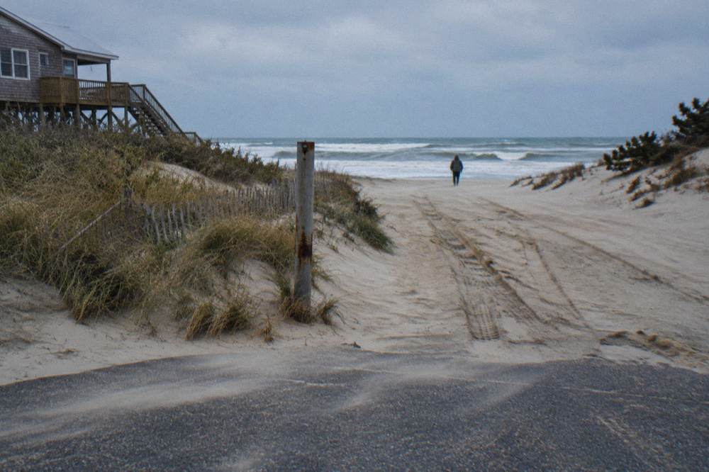 Signpost at the end of a paved road with sand continuing beyond it toward the ocean