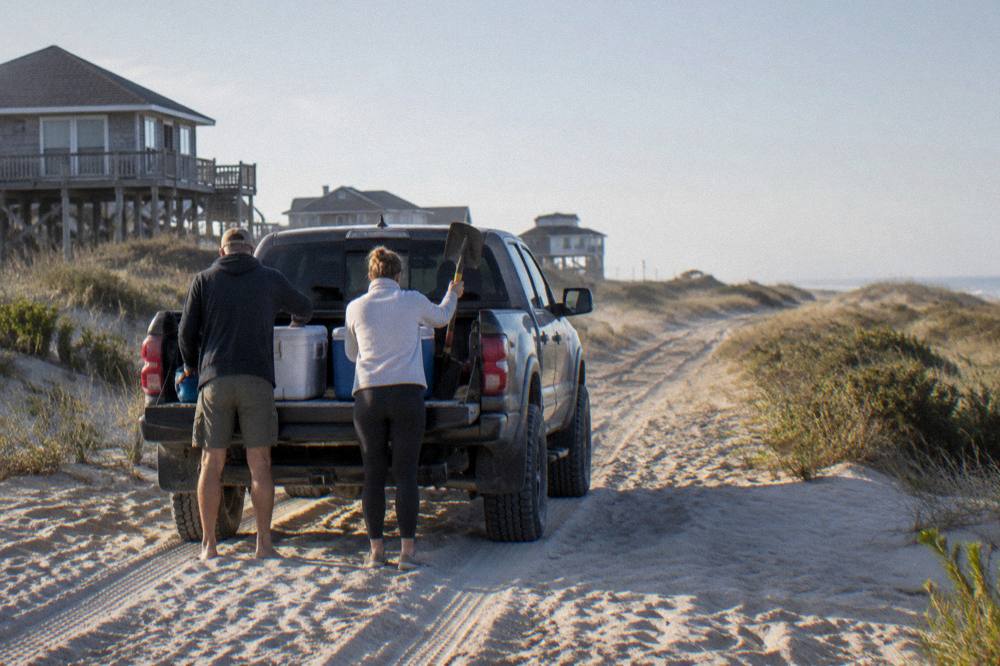 Family loading gear into the back of a four-wheel-drive truck on a sandy beach track
