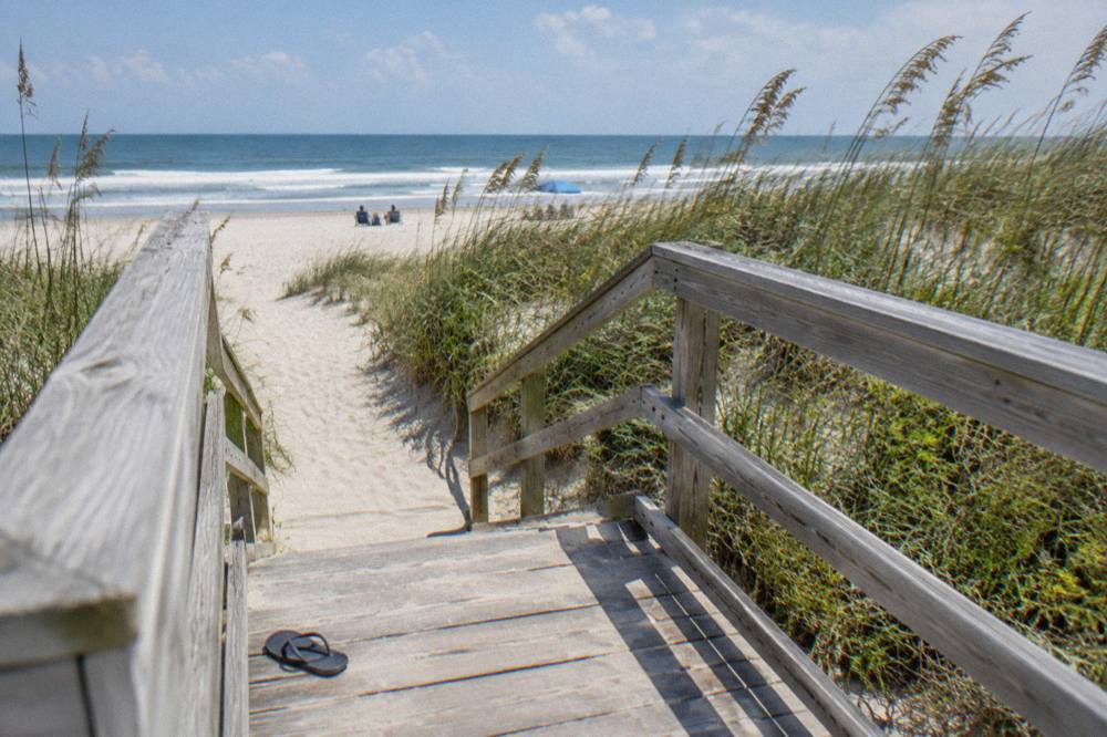 Wooden dune walkover leading to a wide sandy beach beside sea oats