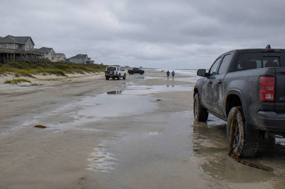 Four-wheel-drive trucks parked along a wide northern beach at low tide