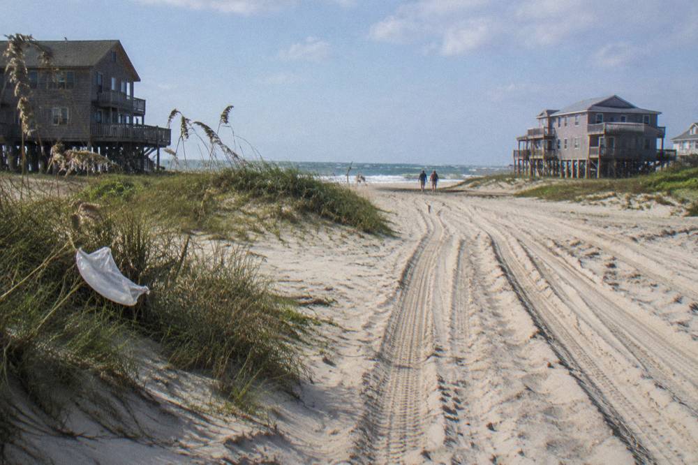 Open sandy beach with tire tracks leading toward distant dune lines
