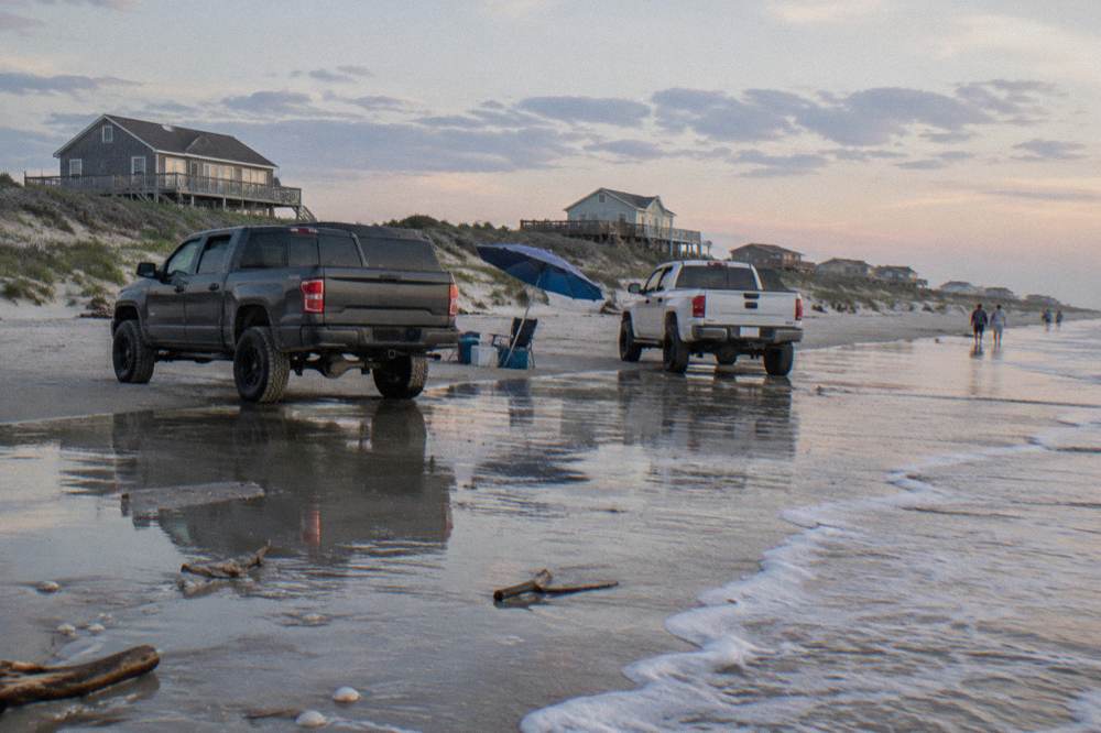 Four wheel drive trucks parked on wet sand at the base of a wide open beach