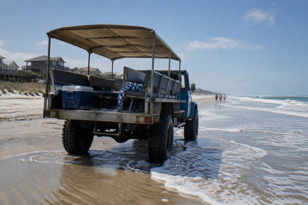 Open-air four-wheel-drive truck on hard sand at the edge of the surf