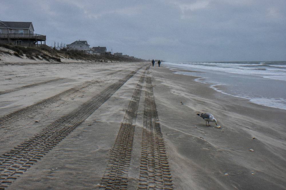 Wide empty beach north of Corolla with tire tracks in the sand and ocean on the horizon