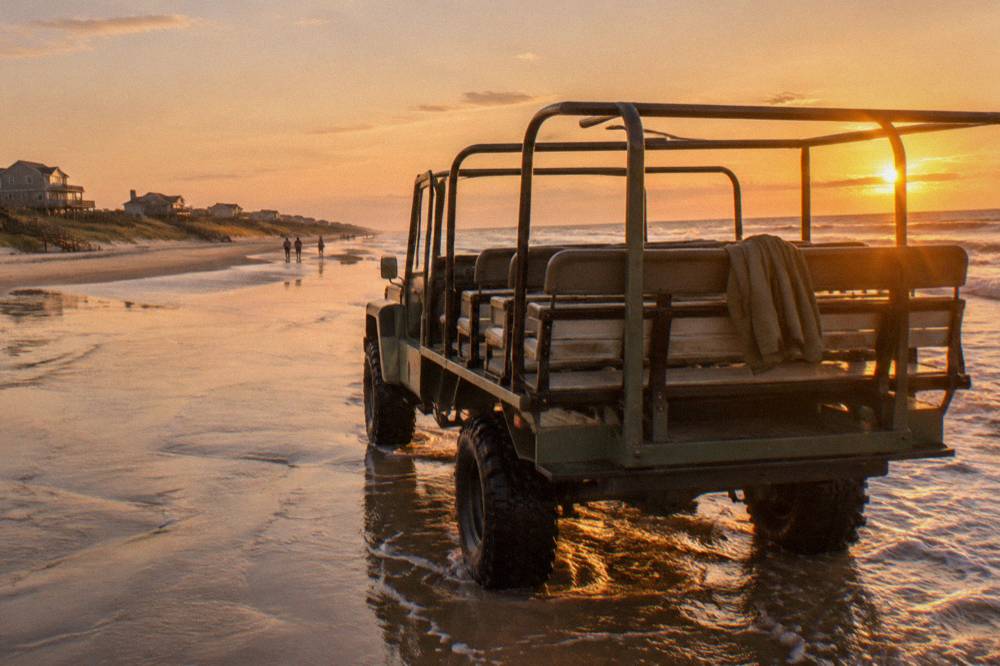 Parked open-air four wheel drive truck on hard sand at the edge of the surf
