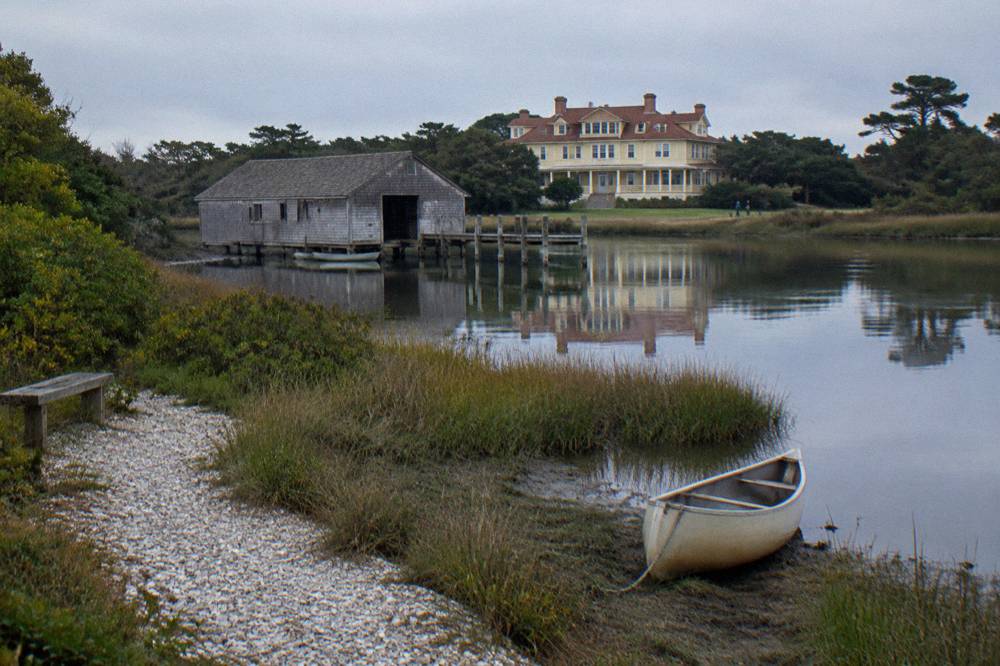 Yellow art deco club house beside calm sound water with a boathouse in front