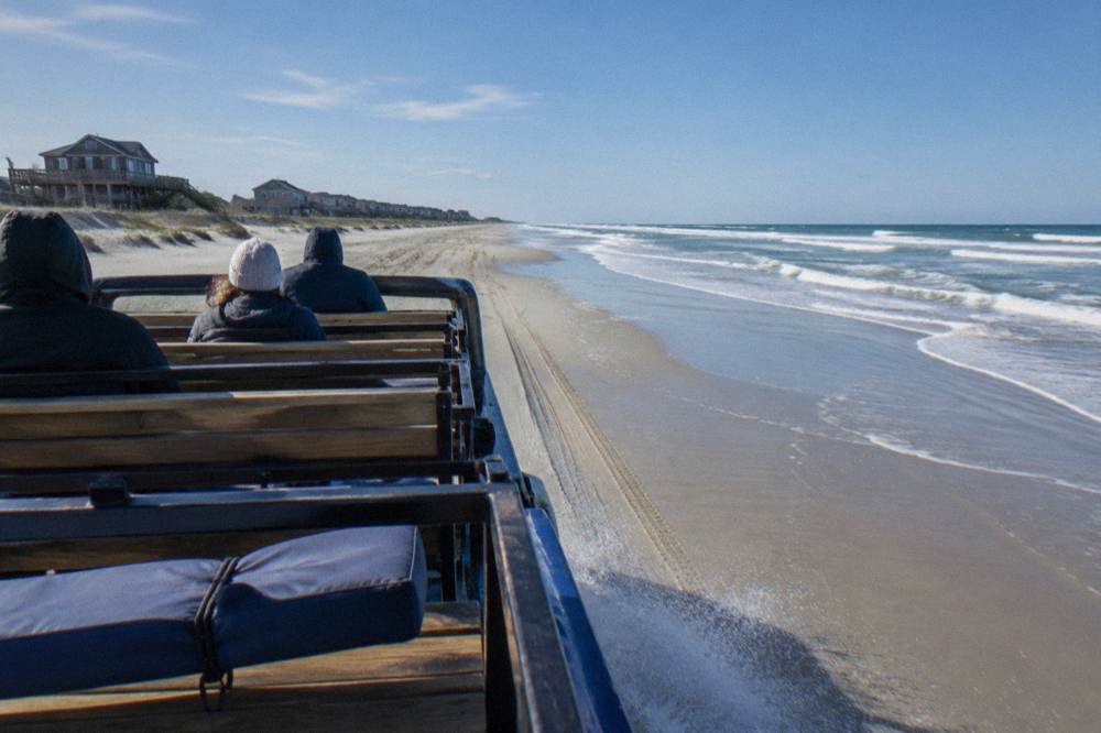 Open air four wheel drive truck driving along a wide wet sand beach