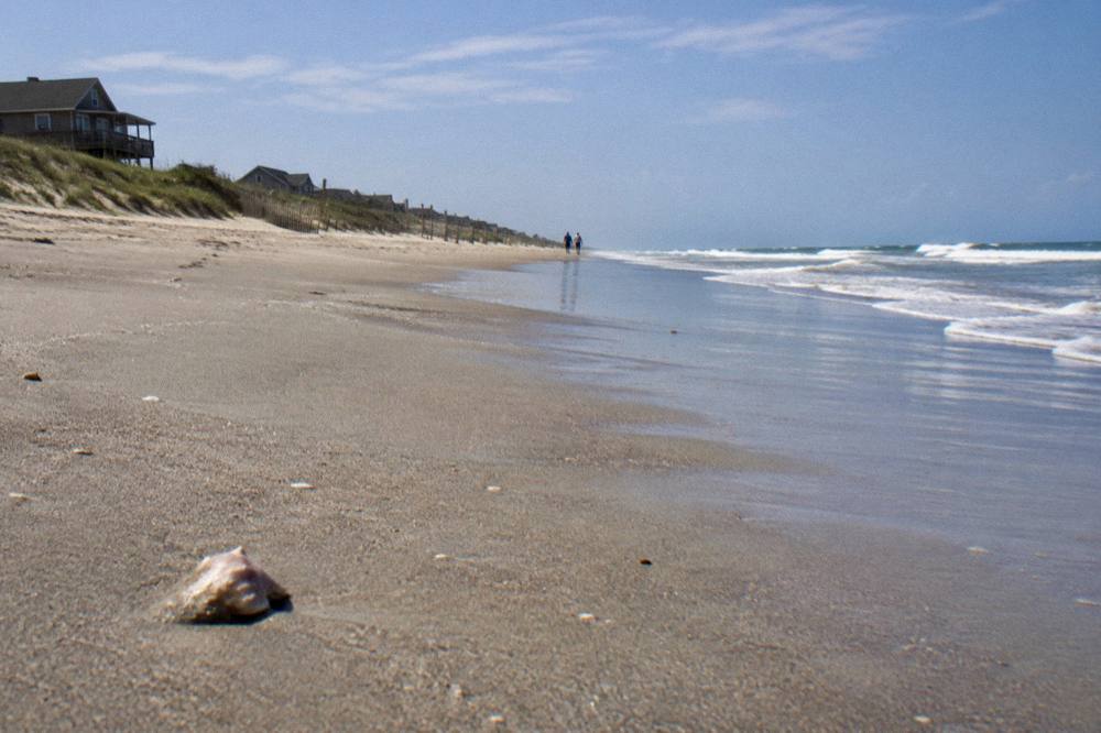 Endless wet-sand beach stretching toward the horizon with a distant fence line and ocean waves