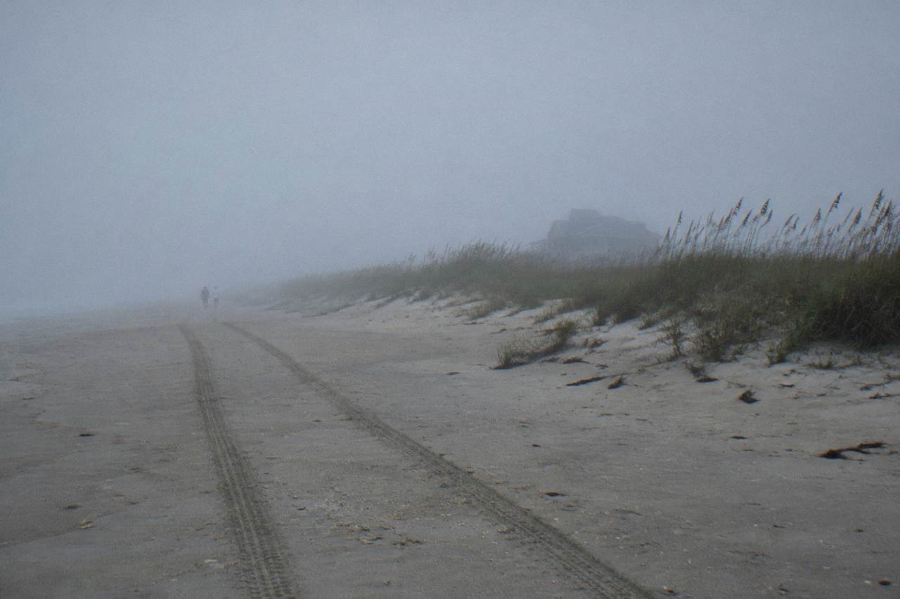 Wide empty beach at the northern end of the Outer Banks with tire tracks in the sand and low dunes under a hazy sky