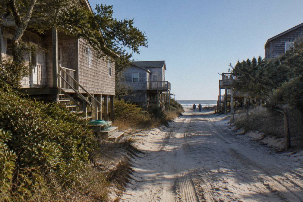 A dirt sand road running between weathered beach houses toward the open beach