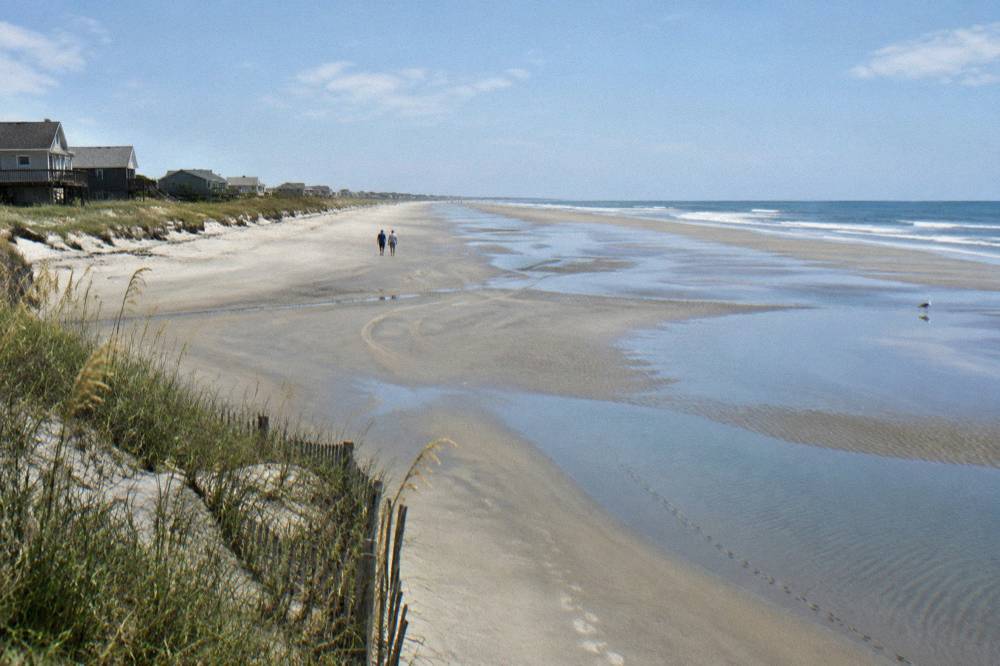 A wide empty beach at low tide with tire tracks in the wet sand and dunes behind