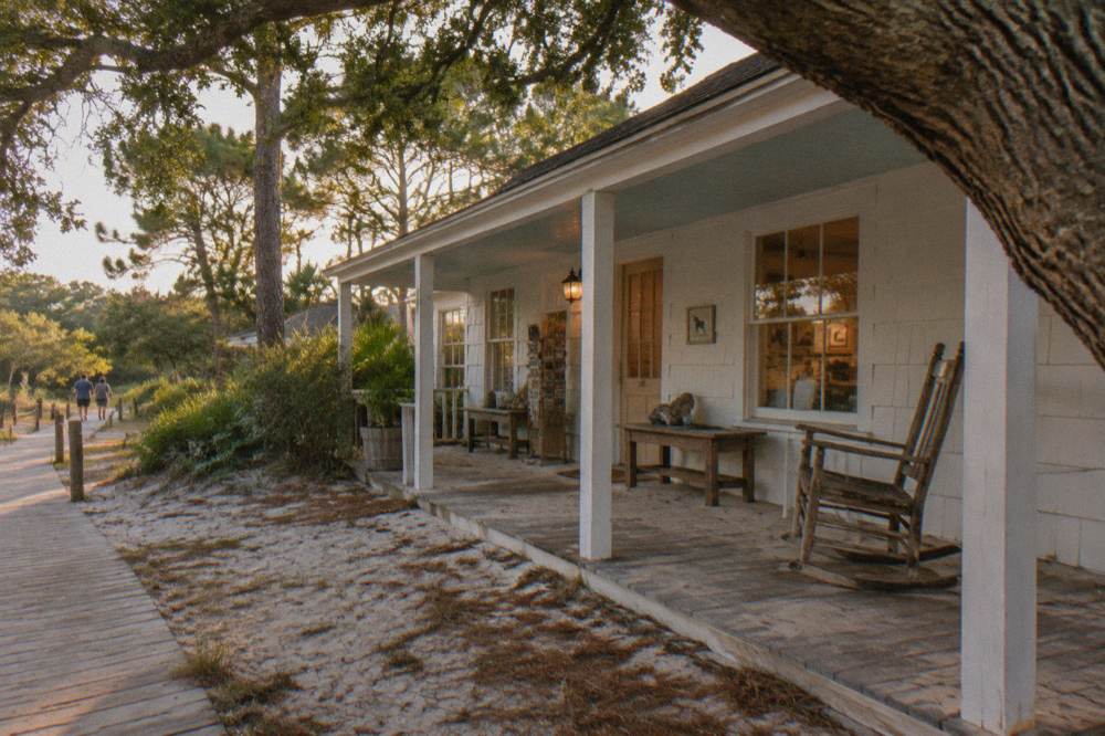 A small white cottage museum with a wooden porch surrounded by maritime forest