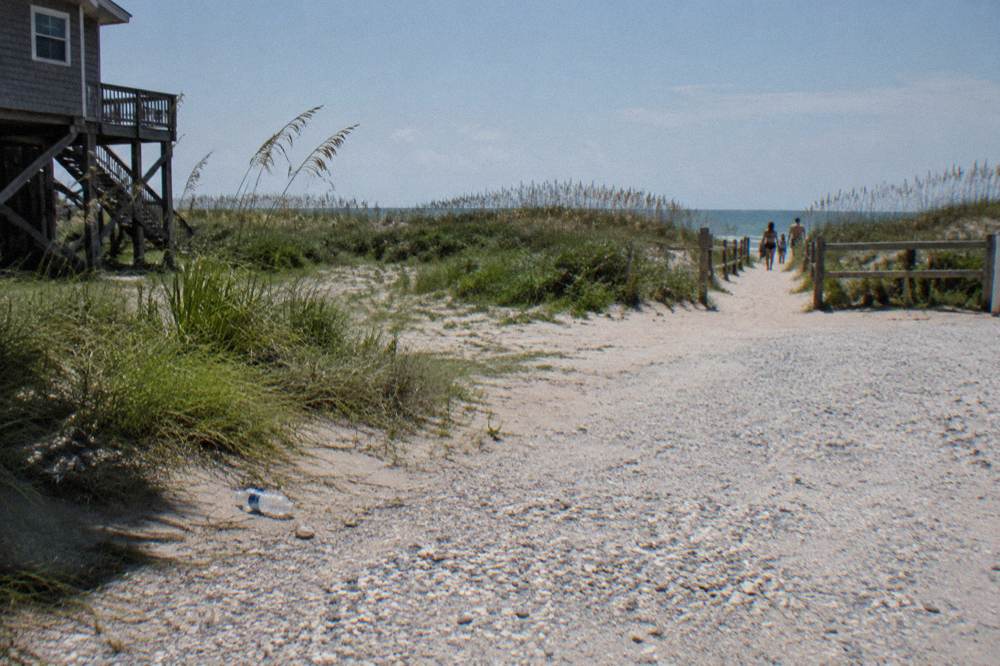 Parking area near Ocean Trail in Corolla with sand paths leading toward dunes and beach grass