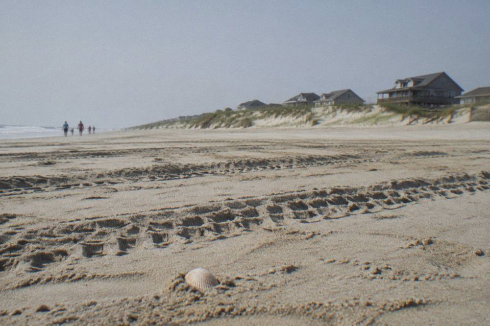 Tire tracks and soft rippled sand on a wide beach with dunes in the distance