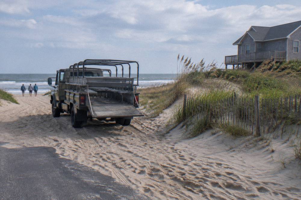Open-air truck with bench seating parked on sand at a beach access point