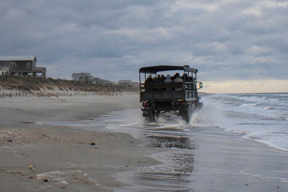 Tour truck driving along firm wet sand at the waterline under open sky