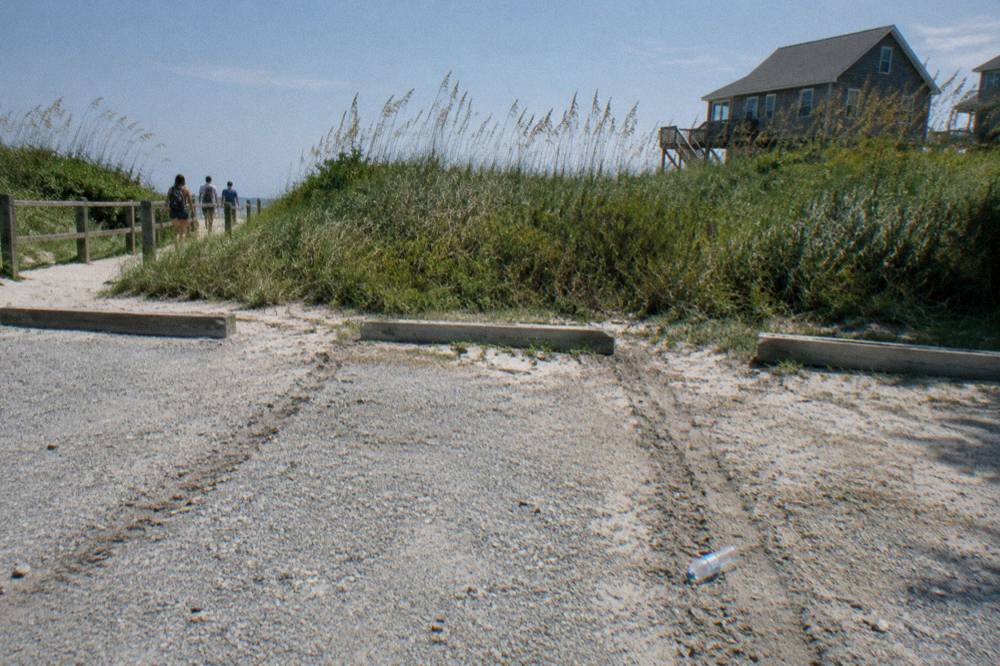 Beach parking area beside a dune with tall grass at the end of the paved road
