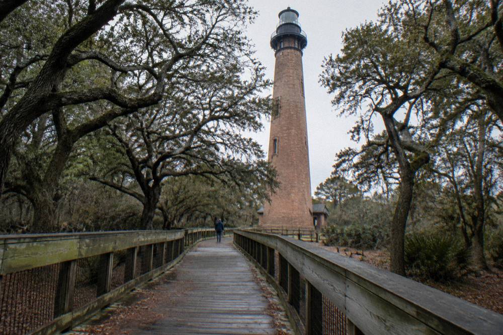 Wooden walkway leading toward a striped lighthouse among maritime trees