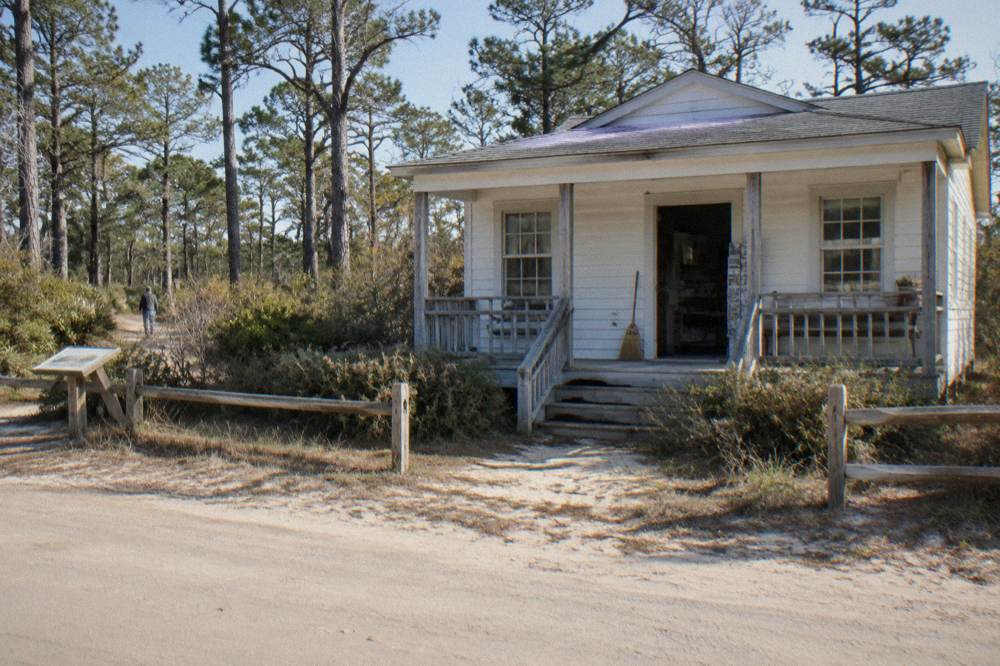 Small white cottage museum building with a wooden porch in a village setting