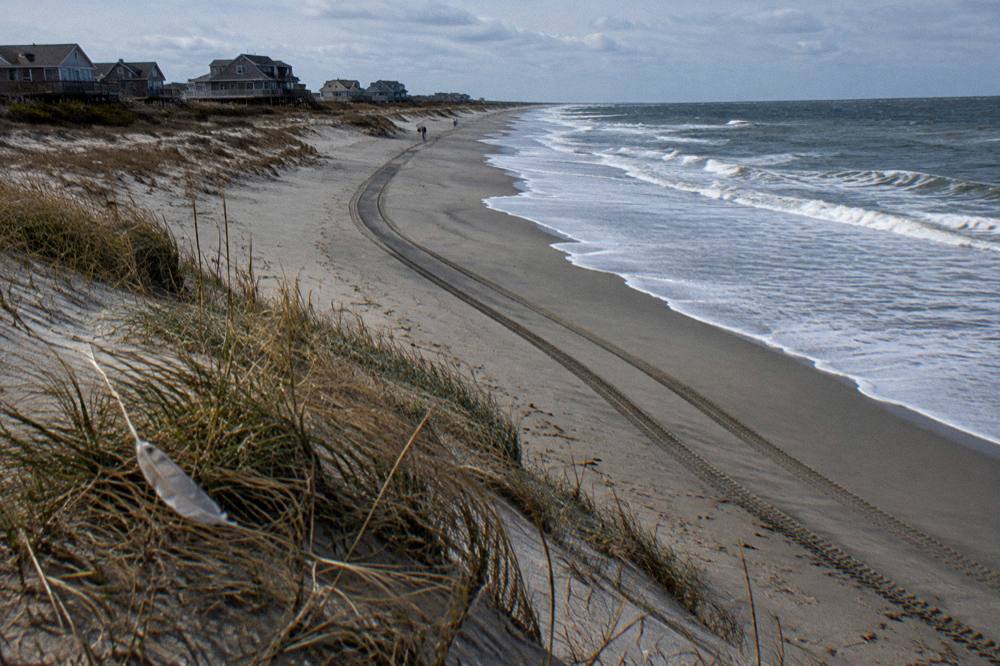 Open-air truck tracks curving along a wide sandy beach toward distant dunes