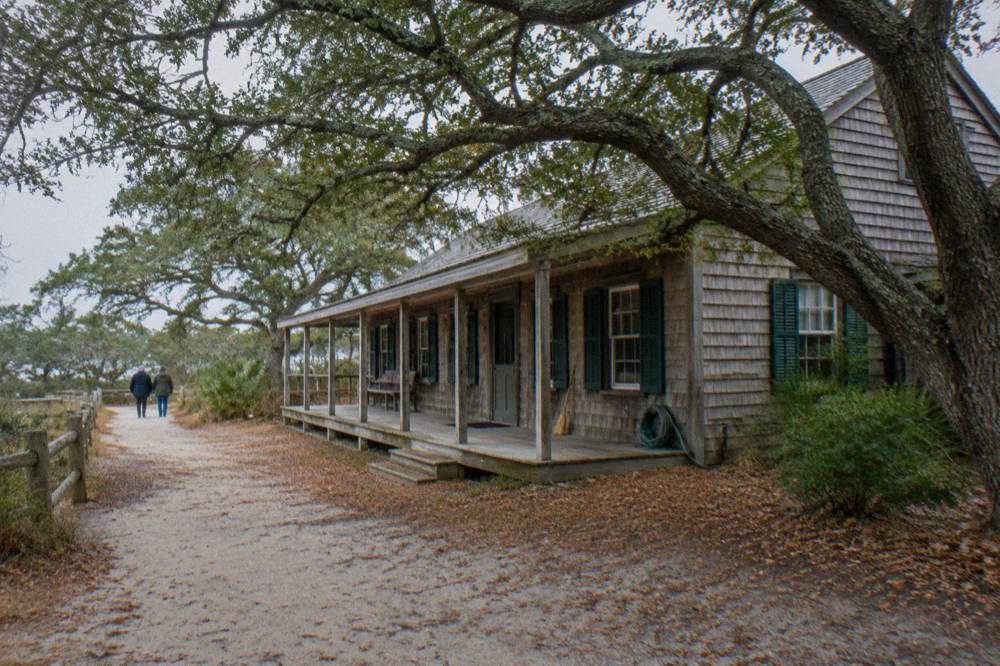 Weathered wooden buildings along a quiet coastal village street with sandy paths