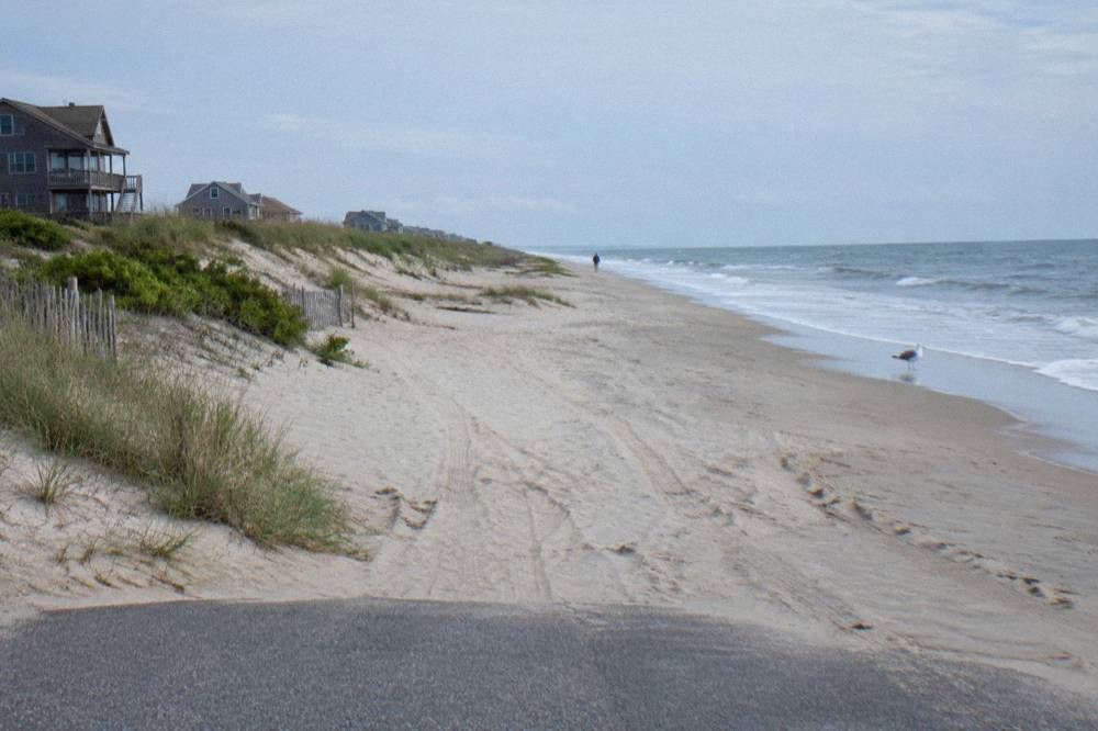 Empty sandy beach stretching north toward low dunes and scattered beach grass