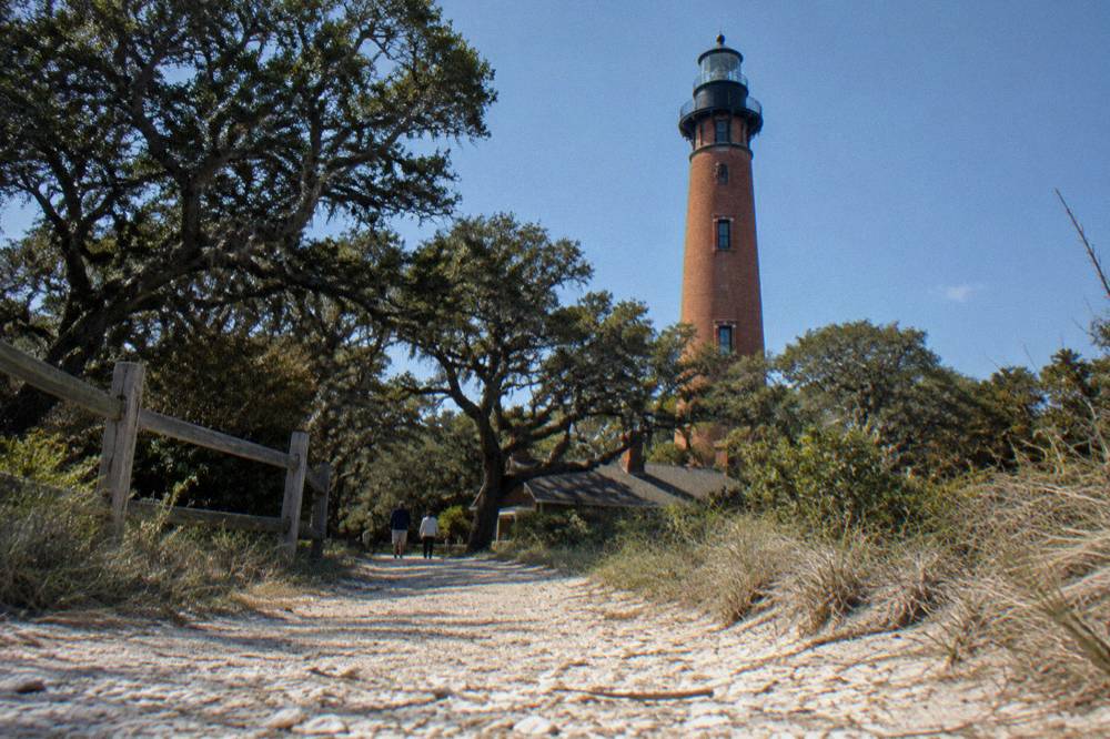 Red brick Currituck Beach Lighthouse rising above low trees under a clear sky
