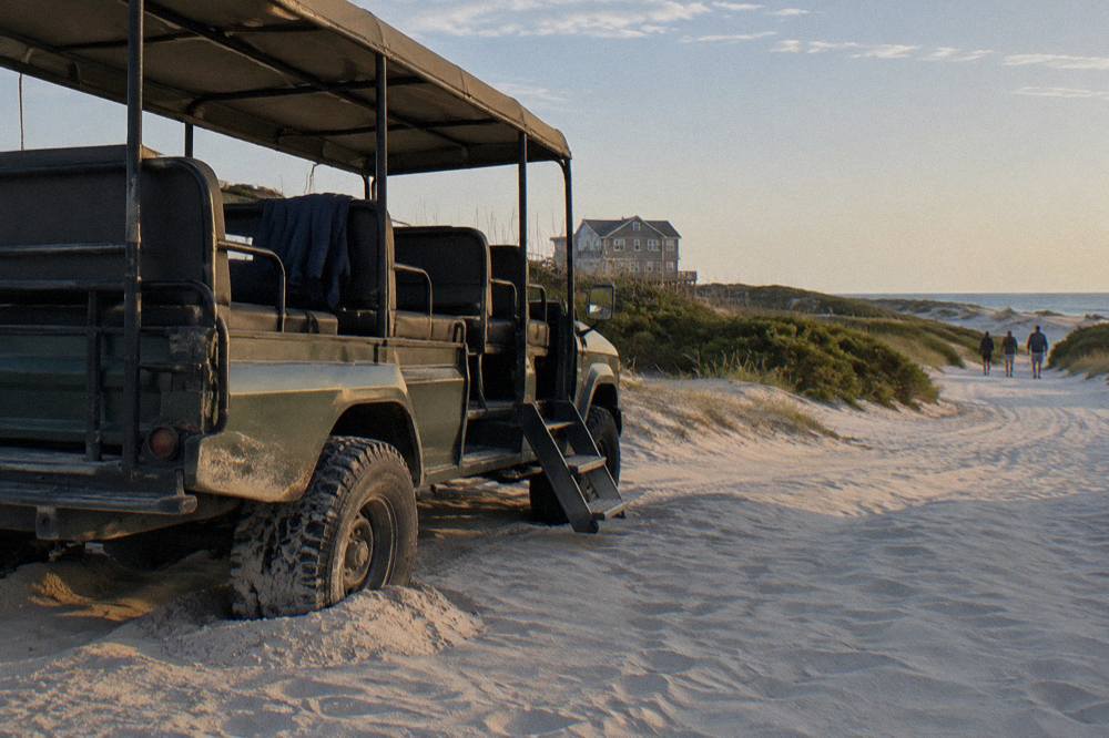 Open-air 4WD tour truck parked on a wide sandy beach beside low dunes
