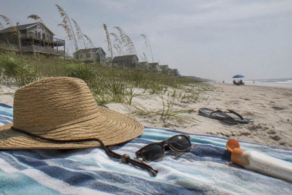 Sunhat and sunglasses resting on a beach towel beside a bottle of sunscreen