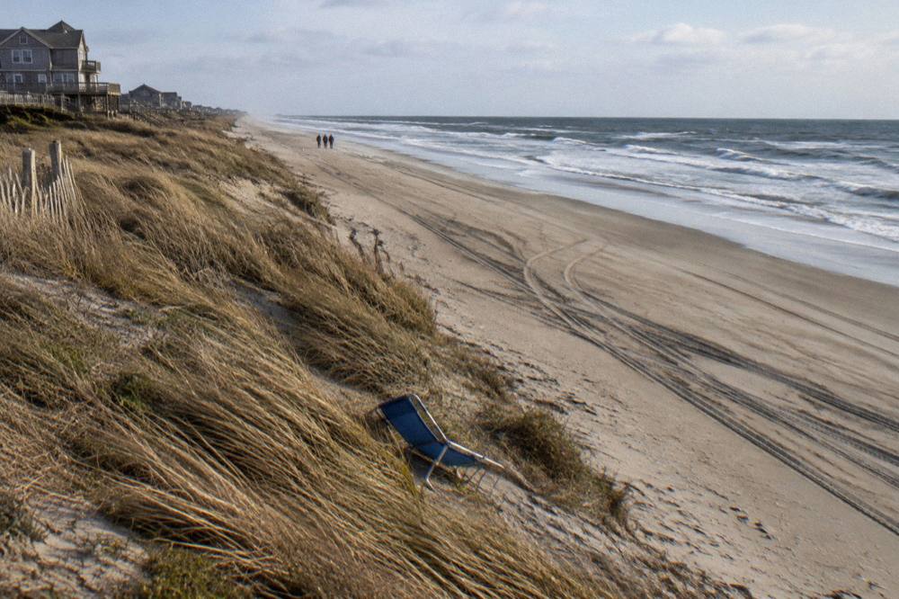 Empty open stretch of northern Corolla beach with tire tracks in the sand and dunes beyond