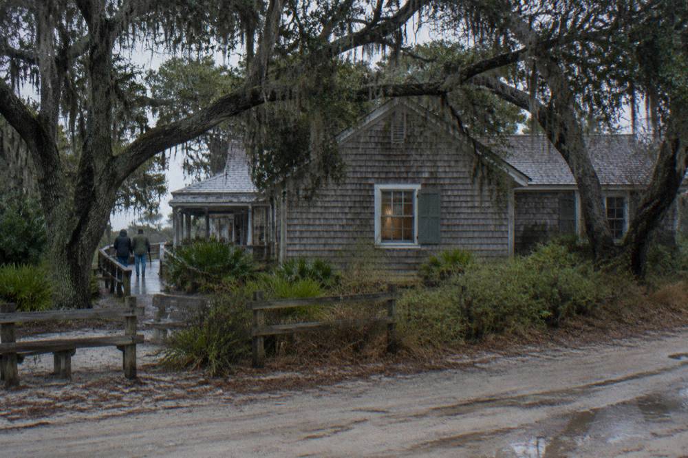 Small weathered museum building surrounded by maritime forest trees in Corolla village