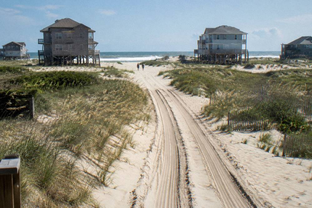 Four wheel drive tracks running north along the wide sand beach toward houses on the dunes