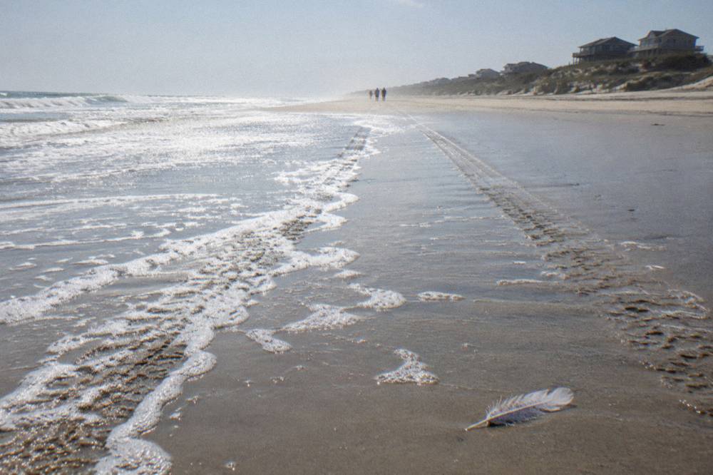 A wide northern Outer Banks beach with tire tracks in wet sand and dunes in the distance